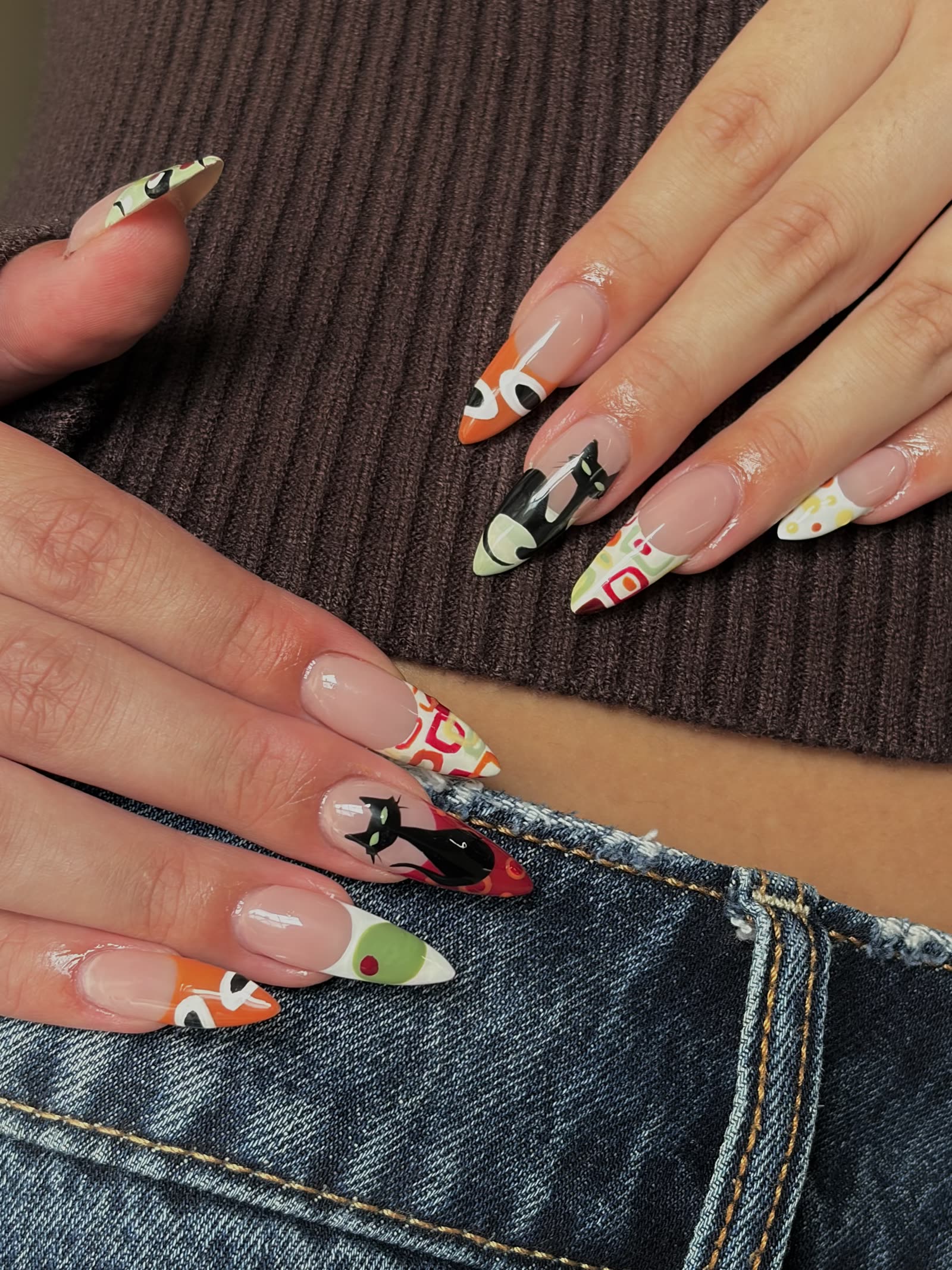 The same hand-painted retro cat set, hands resting against denim and a ribbed brown top