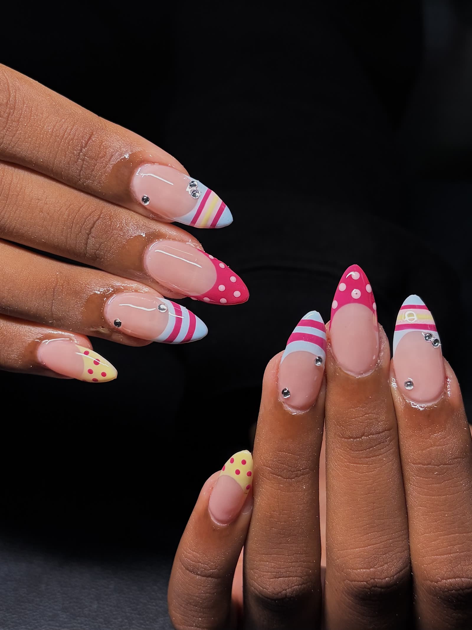 Almond nails with pink, blue and yellow banded and polka-dot tips, set with small rhinestones